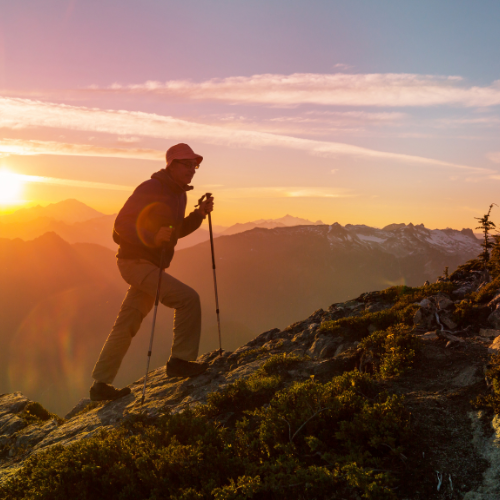 A hiker with walking poles silhouetted against a mountain sunset