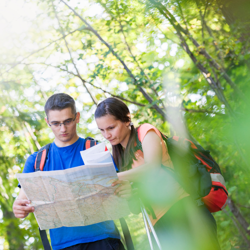 Two hikers checking a paper map together on a woodland trail