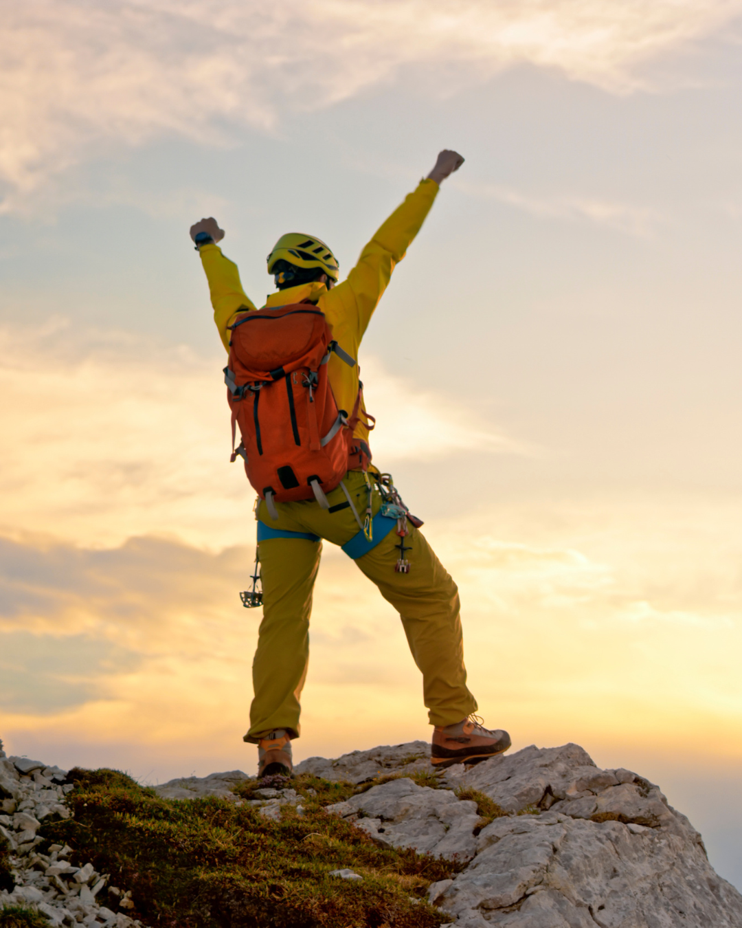 A climber celebrating with arms raised on a mountain summit at sunrise
