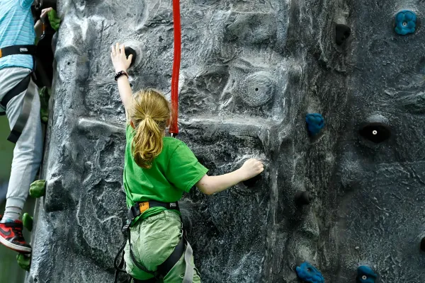 A young climber reaching for a hold on the Climbing Wall at OutdoorXpo