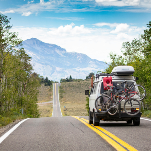 A camper van loaded with bikes on an open road towards mountains