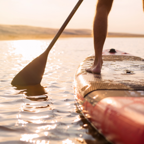 A paddleboarder's feet and paddle on calm water at sunrise