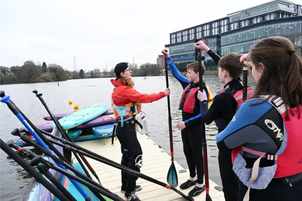 An instructor showing a group of teenagers paddle boarding technique on a lake