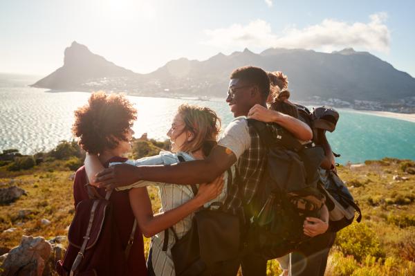 A group of friends embracing on a hilltop overlooking the sea and mountains