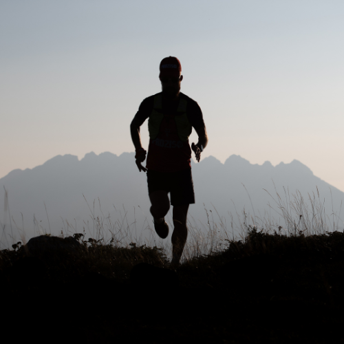 A trail runner silhouetted against mountains at dusk